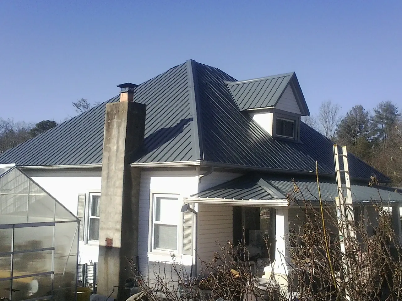 Dark blue standing seam metal roof on a white farmhouse with dormer — Slate & Tile Roof Repair by Roofing Brothers in Davenport