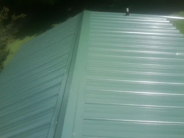 New green metal panels meeting at the ridge of a roof — Flat Roof Repair work by our crew in Davenport